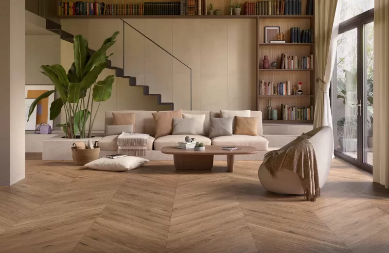 Living room with a sofa in the middle and stairs in the back. Floors has a fake wood look in a chevron pattern.